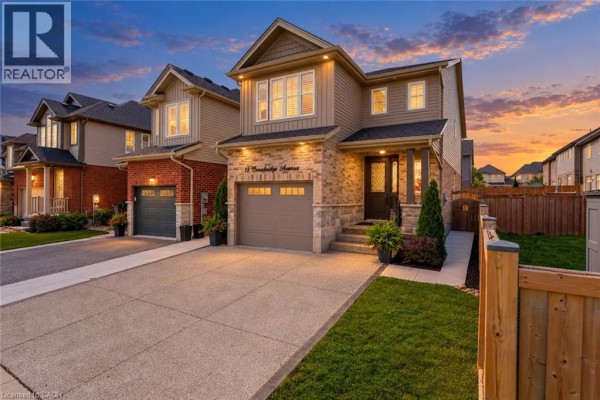 Front exterior of a two-story house at dusk, with warm interior lights illuminating the windows. - 18 Crossbridge Avenue, Kitchener