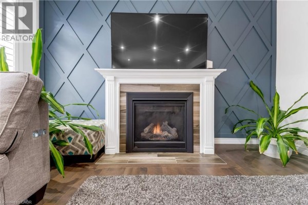 Living room fireplace with a white mantel, blue geometric wall paneling, and a large television above. - 18 Crossbridge Avenue, Kitchener