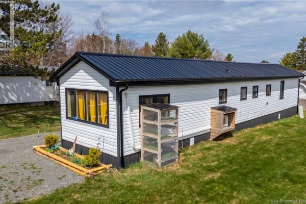 Side exterior view of a white vinyl-sided mobile home with a black metal roof and a wooden garden structure. - 18 Daisy Lane, Riverview