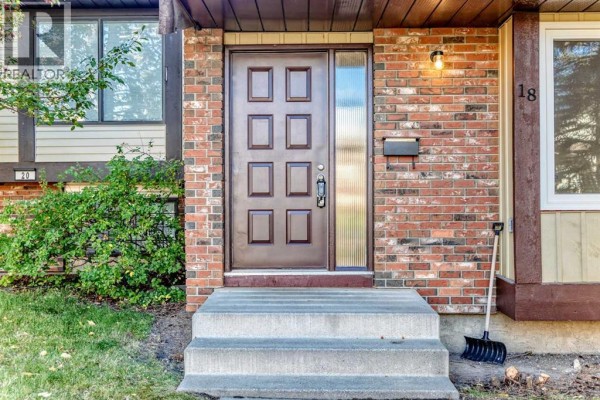 Close-up of the brown front door with a glass panel, brick facade, and house number 18. - 18 Dalhousie Crescent Nw, Calgary