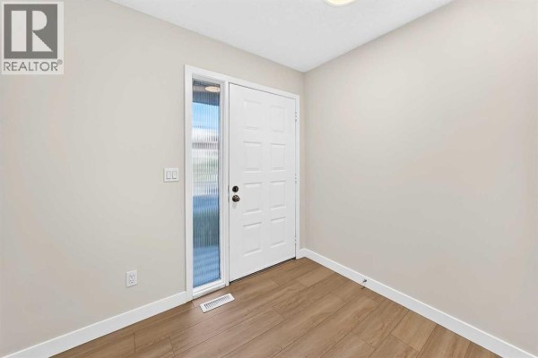 Interior entryway with a white door, a narrow sidelight window, and light wood-look laminate flooring. - 18 Dalhousie Crescent Nw, Calgary