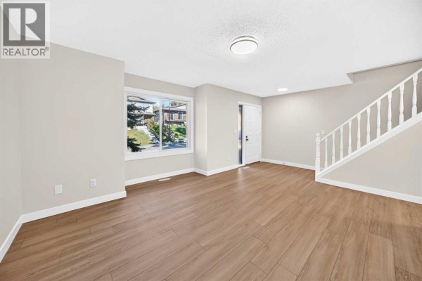 Living room with light grey walls, wood-look flooring, a large window with a view, and white stairs. - 18 Dalhousie Crescent Nw, Calgary