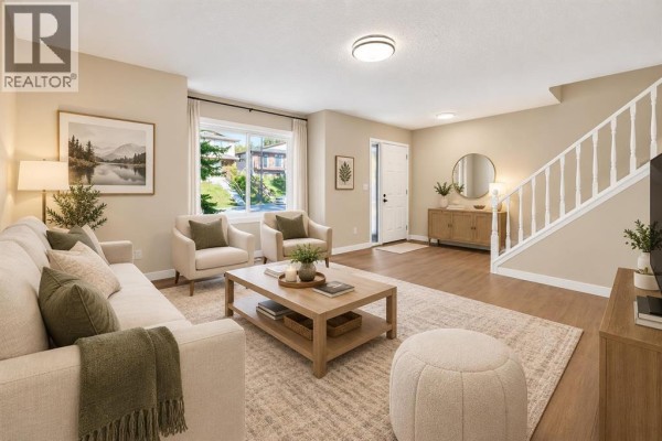 Spacious living room with light grey walls, wood-look flooring, and a staircase leading upstairs. - 18 Dalhousie Crescent Nw, Calgary
