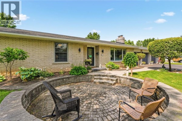 Circular paved patio with stone retaining walls and seating, facing the brick ranch-style house. - 18 Fireside Drive, Flamborough