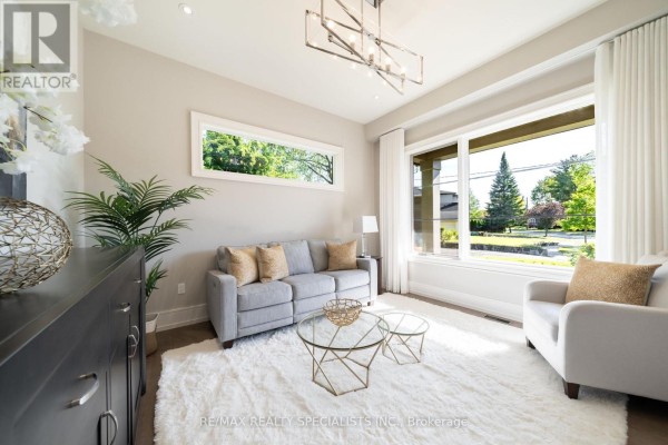Living room seating area with a grey sofa, armchair, coffee tables, and large windows with drapes. - 18 Florence Drive, Oakville