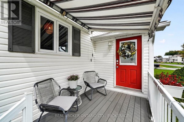 Covered front porch with grey deck, white railing, and red front door. - 18 Frost Avenue, South Stormont