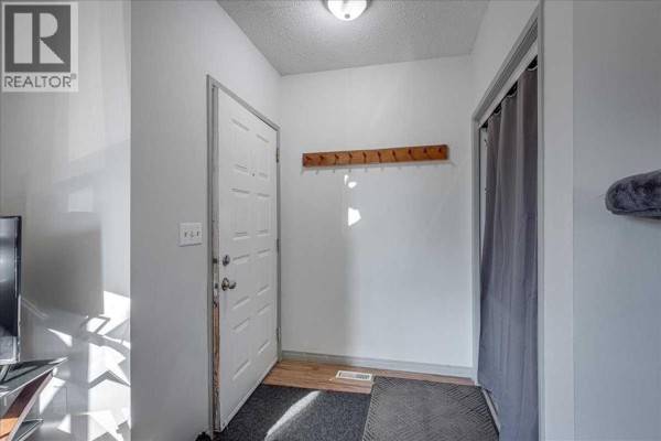 Interior entryway with white doors, a coat rack, and grey mats on a wood-look floor. - 18 Greenham Drive, Red Deer