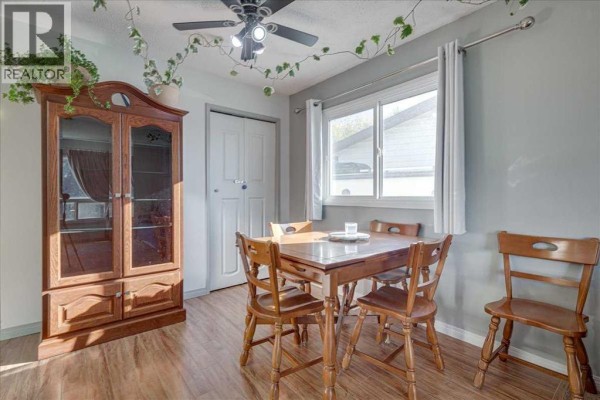 Dining area with a wooden table and chairs, a glass-doored china cabinet, and a window overlooking the exterior. - 18 Greenham Drive, Red Deer