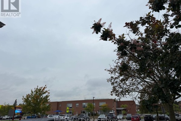 View of a brick building with trees and cars in the foreground against an overcast sky. - 18 Harkins Drive, Ajax