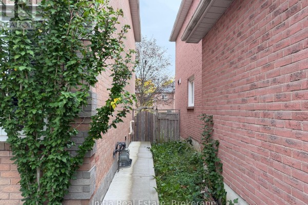Narrow side yard with concrete walkway between two brick houses, leading to a wooden fence. - 18 Harkins Drive, Ajax