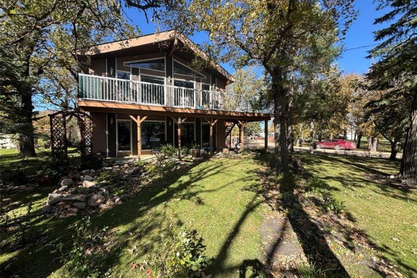 Side view of a two-story house showing a raised wooden deck with glass railings and a lower-level patio. - 18 Hawthorne Drive, Killarney