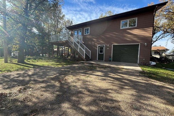 Covered concrete patio on the lower level of a brown wood-sided house with large windows and a propane tank. - 18 Hawthorne Drive, Killarney
