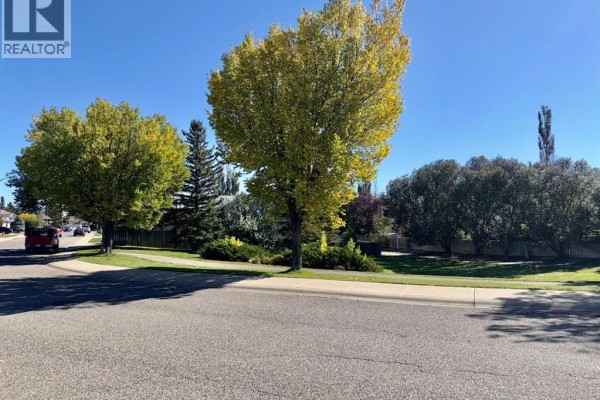 Street view showing mature trees with yellow and green foliage lining a paved road in a residential neighborhood. - 18 Heritage Close W, Lethbridge