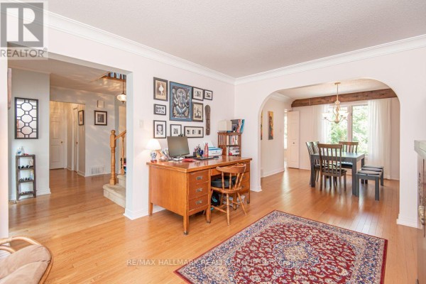 Living room with a wooden desk, bookshelves, and an archway leading to a dining area with a table. - 18 Hesse Crescent, Ottawa