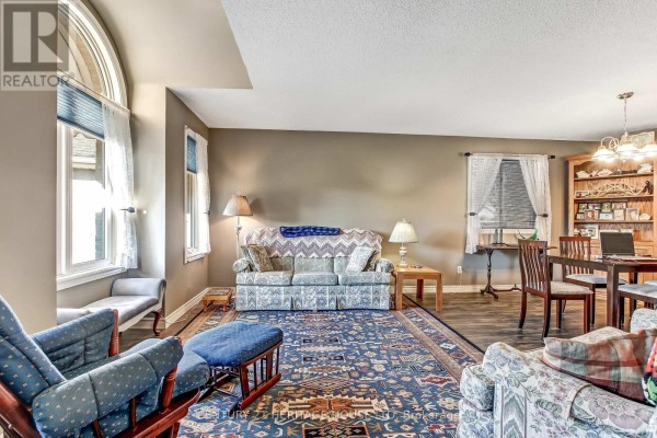 Living room with a floral sofa, patterned rug, and large arched window. - 18 Hickory Boulevard W, Strathroy Caradoc