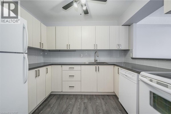 L-shaped kitchen with white cabinets, grey tiled backsplash, and stainless steel sink. - 18 Holborn Court Unit# 211, Kitchener