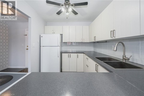 U-shaped kitchen with white cabinets, stainless steel sink, and a white refrigerator. - 18 Holborn Court Unit# 211, Kitchener