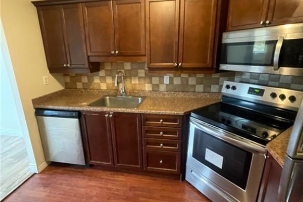 Kitchen with dark wood cabinets, granite countertops, stainless steel appliances, and a tiled backsplash. - 18 Holborn Court Unit# 212, Kitchener