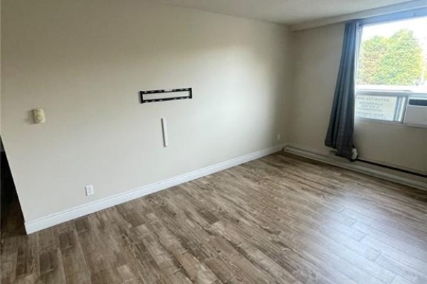 Living room with light wood laminate flooring, beige walls, and a wall-mounted TV bracket. - 18 Holborn Court Unit# 212, Kitchener