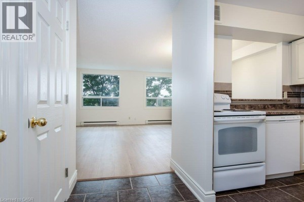 View from apartment doorway into living room with two windows and adjacent kitchen area. - 18 Holborn Court Unit# 409, Kitchener