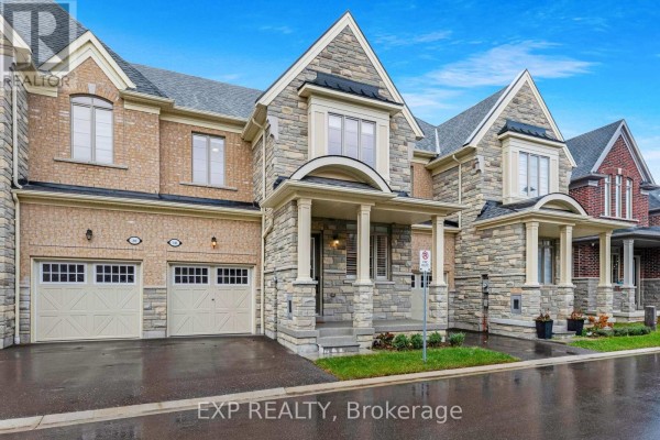 Front exterior view of a brick and stone townhouse, showing garages and entrance. - 18 Hough Lane, Ajax