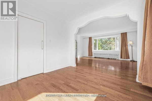 View of a living room from an adjacent hallway, showing hardwood floors and a large arched doorway. - 18 Irvington Crescent, Toronto