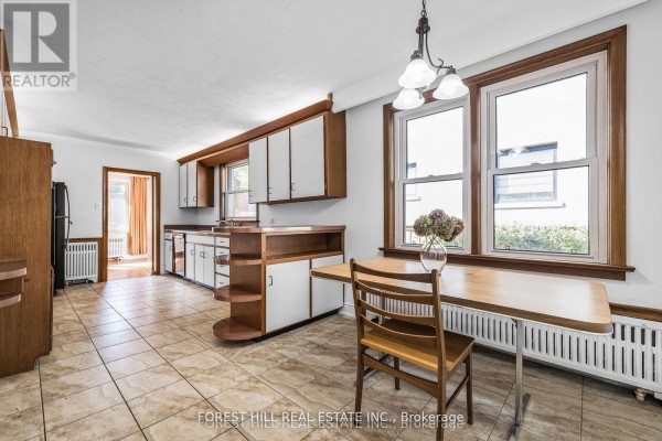 Kitchen with light-colored cabinets, beige tiled floors, a wooden table, and chairs. - 18 Irvington Crescent, Toronto