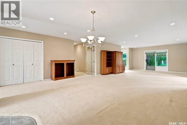 Spacious living and dining area with neutral carpeting, mirrored closet doors, wooden cabinetry, and a chandelier. - 18 Lakeview Place, Regina