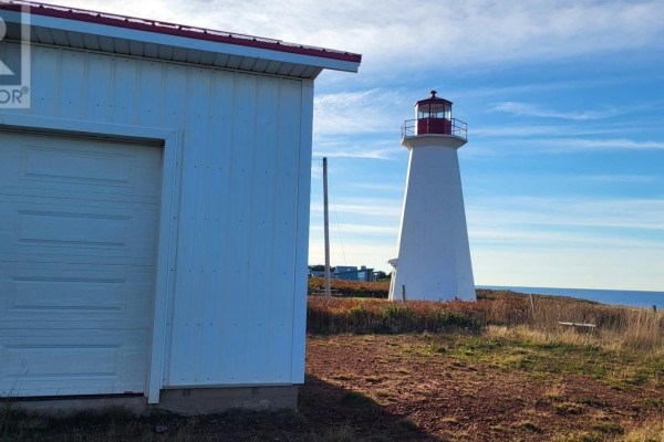 View of the ocean from a grassy yard, with a white building in the foreground and a lighthouse in the distance. - 18 Light House Road, Monticello