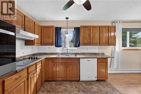 Kitchen with oak cabinets, granite countertops, and a double sink overlooking greenery. - 18 Lobban Avenue, Miramichi
