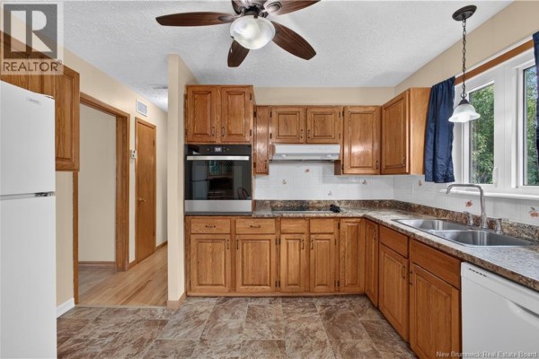 Corner view of a kitchen with oak cabinetry, white appliances, and a patterned floor. - 18 Lobban Avenue, Miramichi