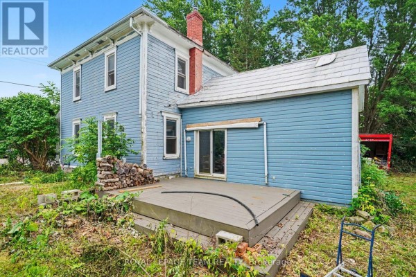 Side exterior view of the blue wooden clapboard house with a covered porch and green foliage. - 18 Moffat Street, North Dundas