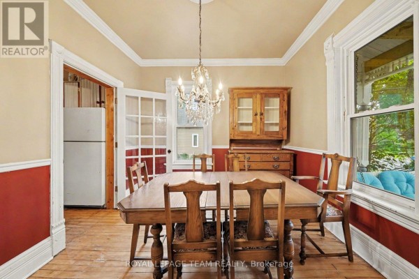Dining room with a wooden table, chairs, cabinet, and a view into a kitchen area. - 18 Moffat Street, North Dundas
