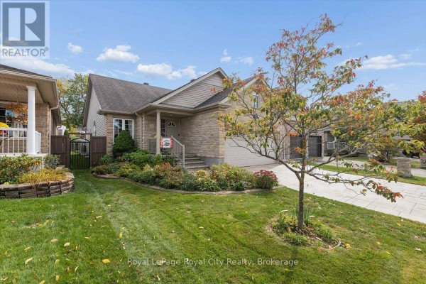 Right-side exterior view featuring the stone house, paved driveway, and a young tree with fall foliage. - 18 Mullin Drive, Guelph
