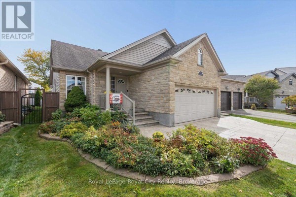 Front view of the house with a covered porch, stone exterior, landscaped garden beds, and a paved driveway. - 18 Mullin Drive, Guelph