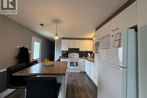 Kitchen with white cabinets, a central island with stools, and wooden flooring. - 18 Parc P'tiso Street, Edmundston
