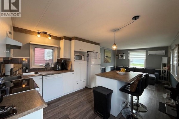 Open-concept kitchen and living area with white cabinetry and a large sectional sofa. - 18 Parc P'tiso Street, Edmundston