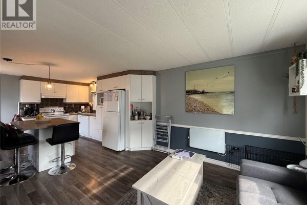 Living area with a grey sectional sofa, a coffee table, and artwork on the wall. - 18 Parc P'tiso Street, Edmundston