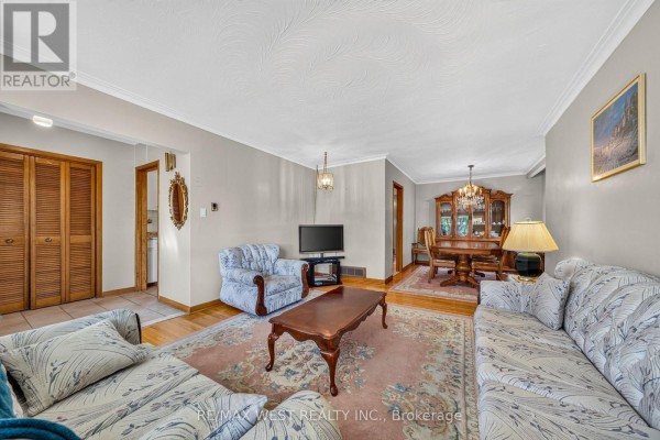 Living room with sofas, armchair, coffee table, TV, and view into dining room. - 18 Pheasant Valley Court, Markham