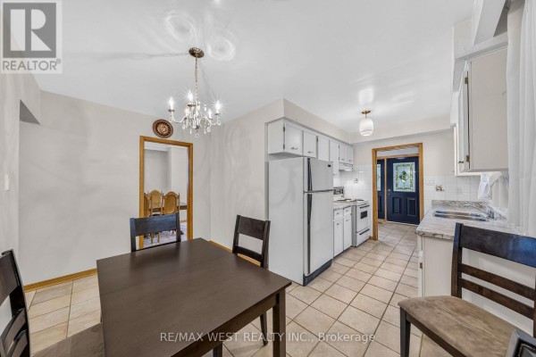 Kitchen with white appliances, cabinets, tile floor, and dining area with dark table. - 18 Pheasant Valley Court, Markham