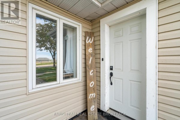 Close-up of a white front door with a 'welcome' sign and adjacent beige siding. - 18 Poyntz Street, Penetanguishene