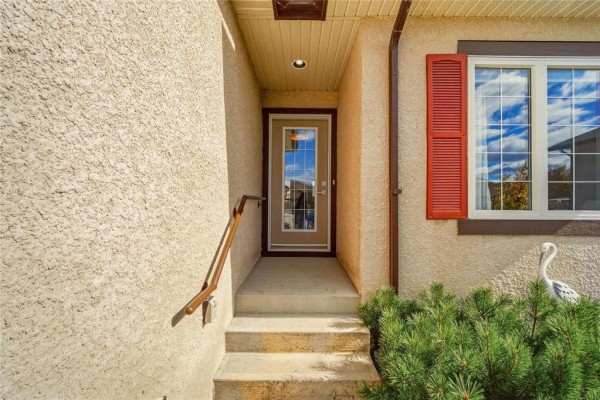 Close-up of the front entrance with a glass door, concrete steps, and red shutters. - 18 Prairieview Cove, Dugald