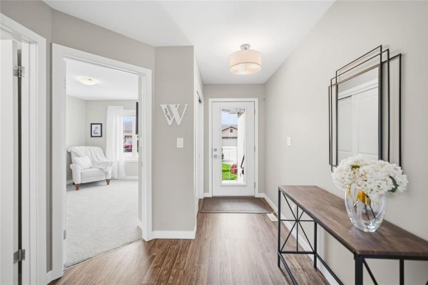 Entryway with wood-look flooring, white doors, a console table, and a mirrored wall. - 18 Prairieview Cove, Dugald
