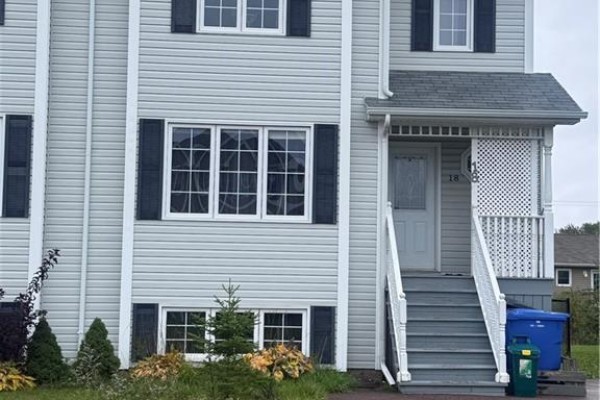 Front facade of a townhouse showing two stories with multiple windows and gray siding. - 18 Rainford Court, Moncton