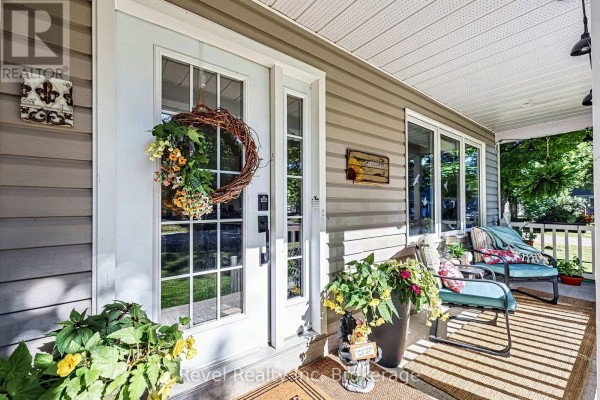 Close-up of a covered front porch with a white door, wreath, chair, and potted plants. - 18 Rue Vanier Road, Tiny