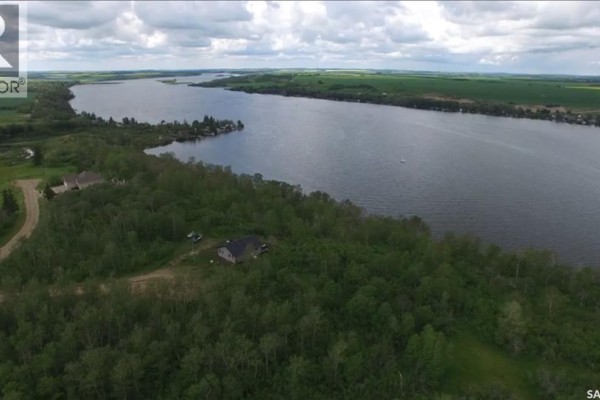 Aerial view of a large lake with forested shoreline and scattered houses, bordered by green fields. - 18 Wakonda Drive, Hoodoo Rm No  401