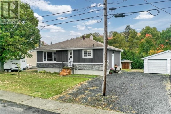 Side exterior view of the grey bungalow with a driveway and detached garage. - 18 Wickwas Street, Onaping