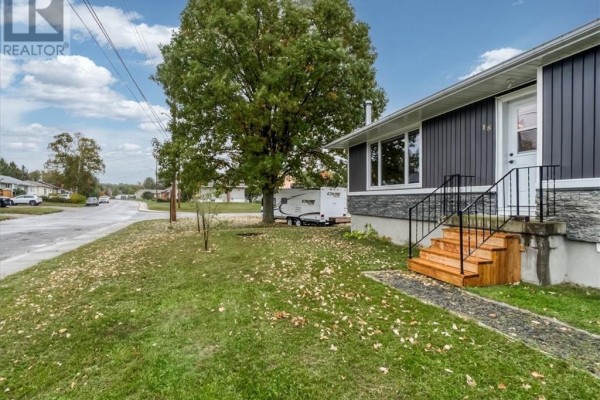 Side yard and front entrance of the bungalow with a trailer parked in the driveway. - 18 Wickwas Street, Onaping