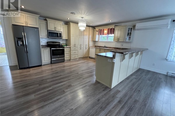 A spacious kitchen with cream-colored cabinets, stainless steel appliances, a large island, and grey laminate flooring. - 18 Wilsonville Avenue, Clarke’s Beach
