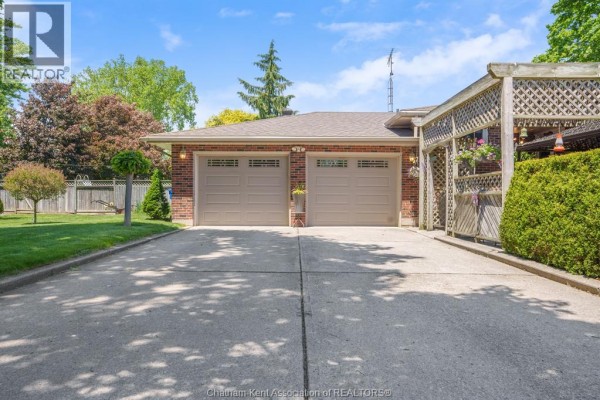Side exterior of a single-story brick house with a green lawn, mature trees, and a paved walkway. - 18 Woodland Avenue, Chatham